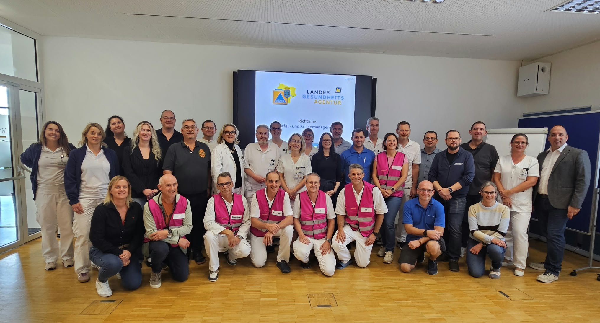 Landesgesundheitsagentur-Mitarbeiter mit Warnwesten und Arbeitskleidung vor Bildschirm in Österreich